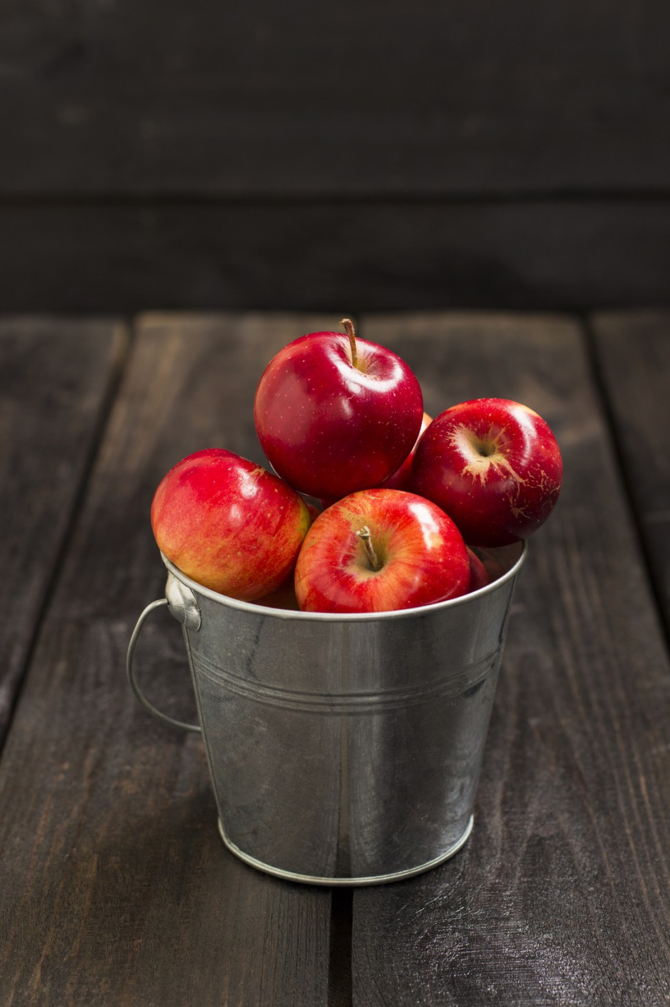 Crop of red apples in metal bucket on a dark wooden background