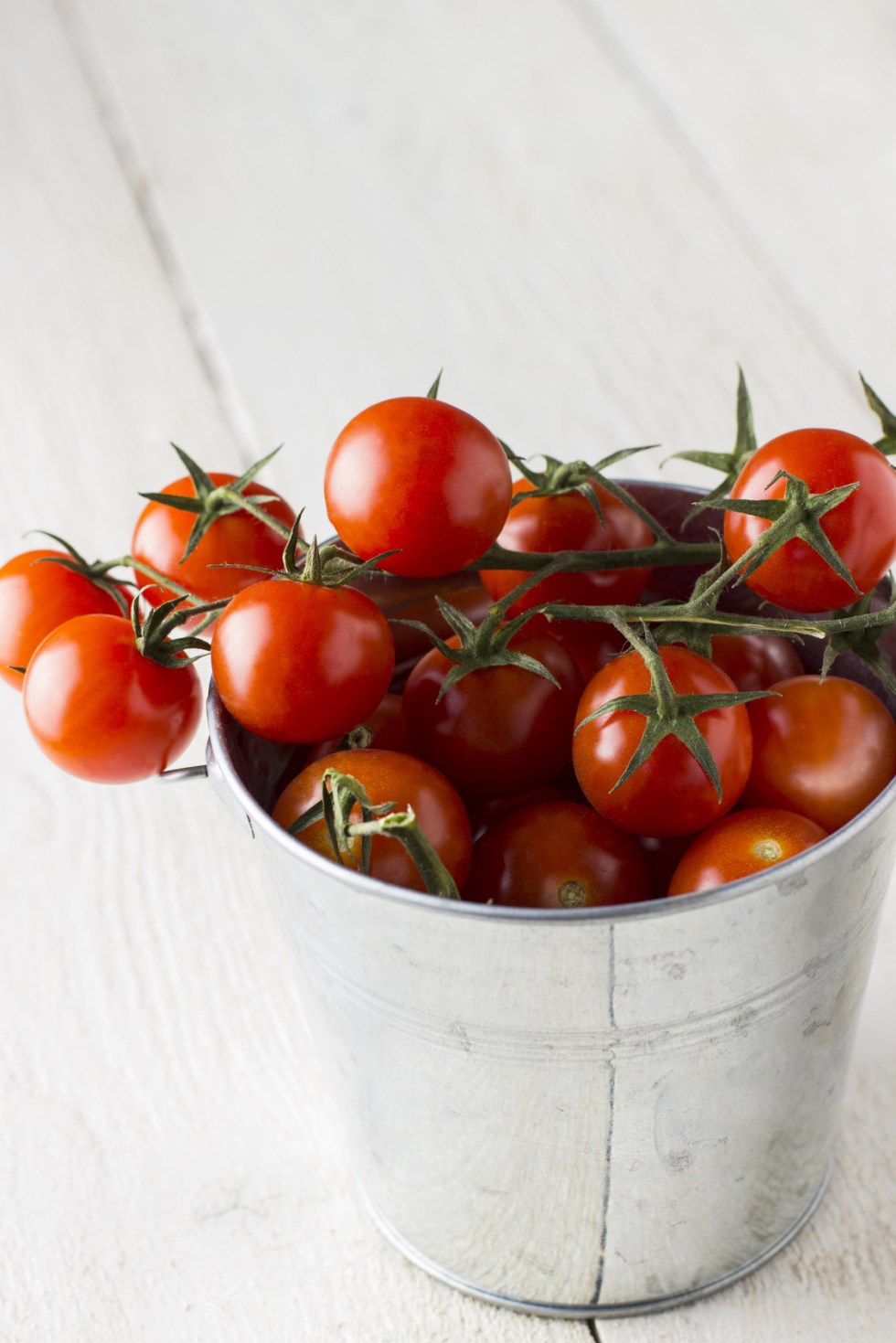 Cherry tomatoes on branch in metal bucket on a wooden background